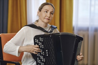 A woman sits comfortably in a chair, skillfully playing the accordion in a well-lit room adorned