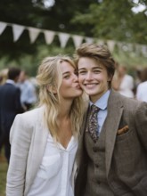A same-sex couple in a suit, one kissing the other on the cheek, surrounded by guests outdoors,