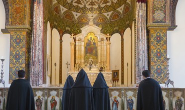 Many monks stand in front of an elaborately decorated altar with bright ornaments, Inside the