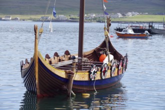 A traditional Viking boat lies decorated in the calm waters of a harbour, Lerwick, Shetland,