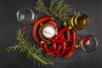 Hot red peppers with vinegar, oil, salt and herbs on a black background