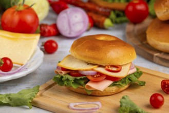 A bagel topped with cheese, sausage, tomatoes, onion and lettuce leaves on a wooden board