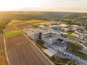 Modern building surrounded by fields and surrounding hills at sunset, new hospital building, Calw