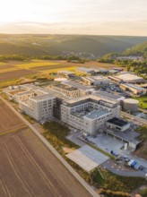 Modern building surrounded by fields and hills at sunset from the air, new hospital building, Calw