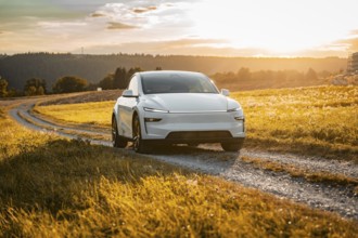 White car on a gravel road through a golden meadow at sunset, Tesla Model Y Juniper, electric car