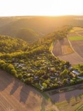 Campsite nestled between fields and wooded hills in the warm sunset light, small town of Perle