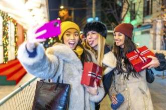 Three happy female friends taking a selfie while holding christmas gifts, enjoying a night out at a