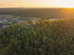 Panoramic shot of a castle ruin in a hilly forest landscape in the warm evening light, small town