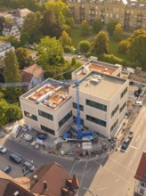 Large modern building under construction with a crane surrounded by an urban environment, small