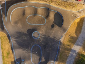 Pump track with blue lines seen from the air, surrounded by shadows and asphalt, pump track,