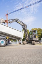 Excavator loading materials into a lorry on a construction site under a clear sky, car park