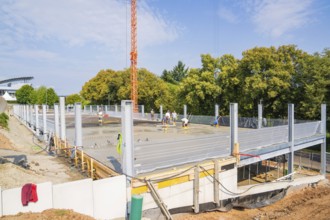 Construction site with metal structures and concrete foundation surrounded by autumnal trees, car