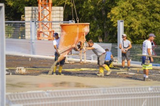 Workers pouring concrete with a shaking bucket on a sunny construction site, car park construction,