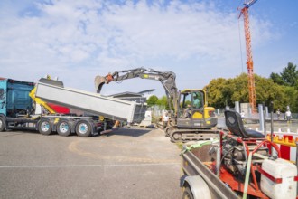 Excavator working on loading a lorry on a construction site, cranes in the background, car park