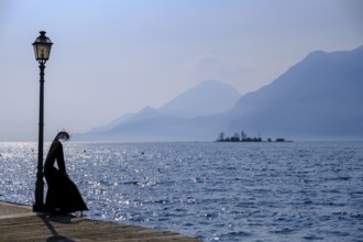 Sculpture of a fisherwoman at the harbour of Cassone di Malcesine, in the background Isole di