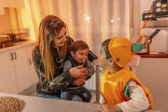 Mother holding baby while older brother wearing pumpkin costume interacting during halloween