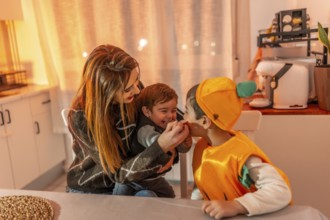 Children wearing pumpkin costumes celebrating halloween joyfully with their mother at home,