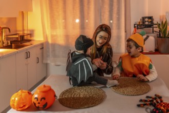 Mother and children wearing halloween costumes are sitting at a table in the kitchen, playing and