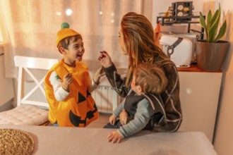 Mom applying halloween makeup on her kid's face, while holding her baby, preparing for trick or