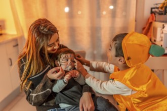 Mother and son applying halloween makeup on baby brother, getting ready for trick or treating
