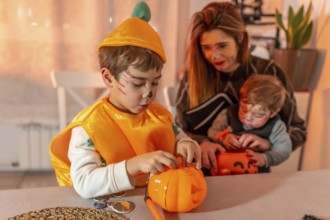 Children wearing halloween costumes are decorating pumpkin baskets with their mother at home