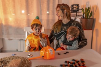 Mother and her two children wearing halloween costumes and makeup, playing with candies on a table