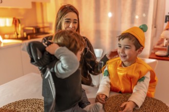 Happy family preparing costumes for halloween party at home, mother helping children wearing bat