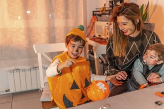 Happy children with painted faces wearing halloween costumes painting pumpkins with their mother at