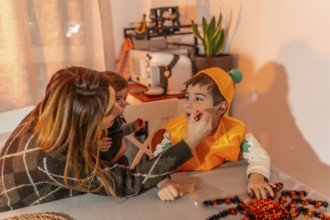 Mother putting halloween makeup on her son, who is wearing a pumpkin costume, while holding her