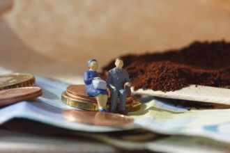 Miniature figure of a married couple sitting on coins and banknotes, ground coffee in a filter bag