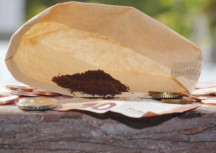 Ground coffee in a filter bag with coins and a ten euro note in front of it, North