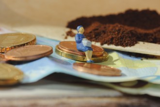 Miniature figure of a woman sitting on coins and banknotes, ground coffee in a filter bag in the