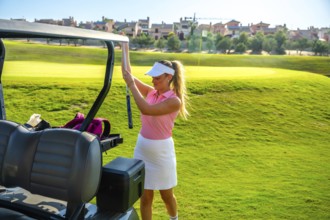 Female golfer placing her golf club into the cart while enjoying a sunny day on a lush green golf