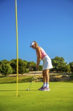 Female golfer putting the ball on the green under a bright sun, showcasing skill and precision on