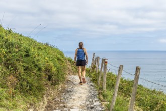 Female tourist walking along a coastal path in zumaia, basque country, enjoying the scenic view of