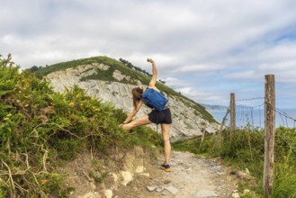 Female hiker stretching leg on a trail overlooking sakoneta beach and flysch cliffs in zumaia,