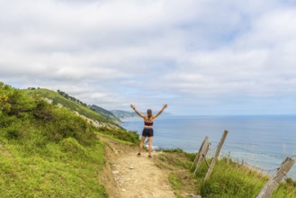 Woman hiker celebrating scenic coastal view with raised arms at sakoneta beach flysch cliffs in