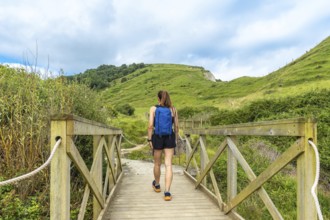 Female tourist with backpack walking on a wooden bridge near sakoneta beach and its flysch in
