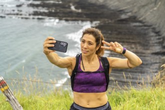 Female hiker taking a selfie with victory sign while hiking along the cliffs of sakoneta beach in
