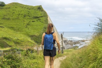 Female tourist walking down a path towards sakoneta beach, enjoying the view of the flysch cliffs