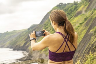 Sportswoman taking photos of the itzurun beach from the sakoneta viewpoint in zumaia, basque