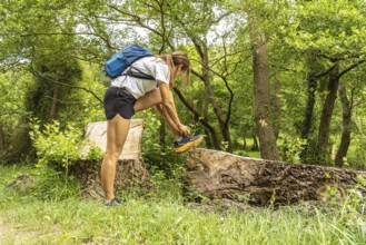Female hiker tying her shoelaces while taking a break on a fallen tree trunk in a vibrant green