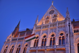 Ornate facade of hungarian parliament building illuminated at twilight with hungarian flag waving,
