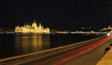 Light trails illuminating road by danube river with hungarian parliament building reflecting on