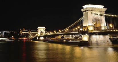 Chain bridge reflecting on danube river with gresham palace in background at night, budapest,