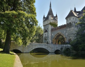Tourists walking over stone bridge leading to vajdahunyad castle reflecting on lake in budapest,