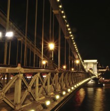 Chain bridge glowing beautifully at night, showcasing blurred car light trails against the backdrop