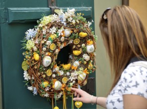 Tourist touching a colorful easter wreath with ceramic eggs and chicks hanging on a green door in