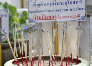 Incense sticks are burning, creating a fragrant smoke, in a pot at a temple in thailand,