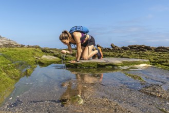Female hiker refreshing with water from a puddle on the flysch rock formations of sakoneta beach in
